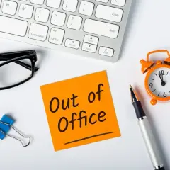 Biurko z okularami, karteczką "Out of Office", zegarkiem i długopisem.
