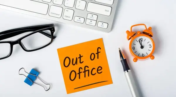 Biurko z okularami, karteczką "Out of Office", zegarkiem i długopisem.